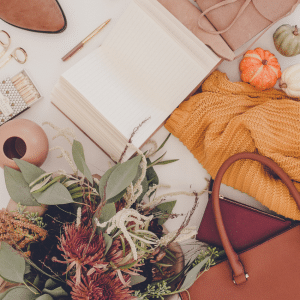 Flat lay lifestyle image featuring warm neutral and Exotic Orange tones including a notebook, flowers, knitwear and accessories, representing brand consistency and cohesive visual identity.