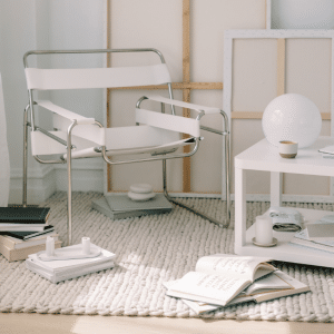 Minimal neutral-toned interior styling featuring a modern white chair, soft textured rug, books and clean Scandinavian-inspired decor in a calm, light-filled space.