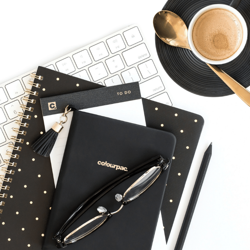 Minimal branding workspace featuring a Colourpac notebook, keyboard, planner, glasses and coffee, representing audience-focused branding, graphic design and business strategy.
