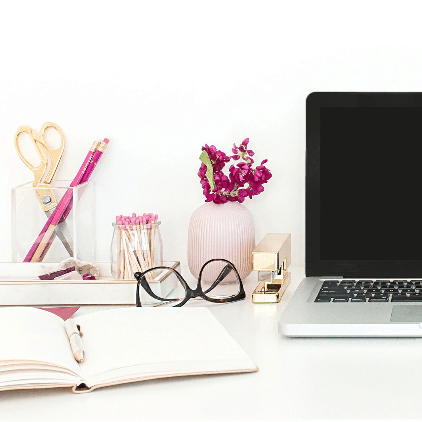 Creative workspace with laptop, open notebook, glasses and pink accessories, representing brand visibility and marketing.